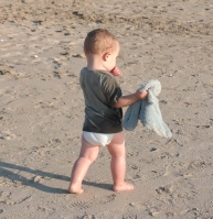Boy on beach holding small soft toy while sucking thumb